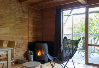 Interior de cabaña de madera en Cahutte de Huttopia Versailles, Francia, con chimenea y terraza acristalada.