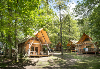 Holzhütten mit Terrassen im grünen Wald bei Cahutte im Huttopia Versailles, Frankreich, im Sommer.
