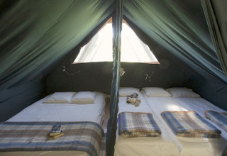 Interior view of the Cahutte at Huttopia Versailles in France, showing two beds with cozy blankets and sunlight.