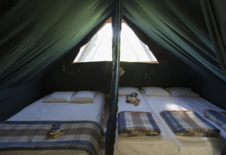 Interior de la cabaña Cahutte en Huttopia Versailles, Francia, con dos camas y mantas acogedoras y luz natural.