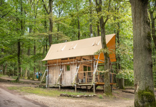 Cabaña Cahutte en Huttopia Versailles, Francia, rodeada de un verde bosque y senderos naturales.
