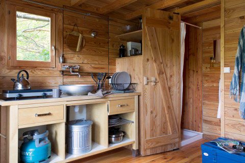 Cozy wooden kitchen interior of Cahutte cabin at Huttopia Versailles, France, featuring a gas stove and sink.