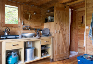 Cozy wooden kitchen interior of Cahutte cabin at Huttopia Versailles, France, featuring a gas stove and sink.