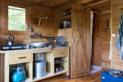 Acogedora cocina de madera de la cabaña Cahutte en Huttopia Versailles, Francia, con hornillo de gas y fregadero.