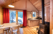 Gemütliche Glamping-Unterkunft mit Holzmöbeln, Kaminofen und Blick auf verschneiten Wald draußen.