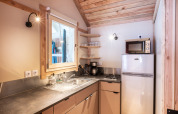 Lyst glampingkøkken med træloft, vindue, komfur, køleskab, mikrobølgeovn og åbne hylder.