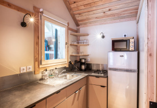 Acogedora cocina de glamping con techo de madera, ventana, refrigerador, microondas y estufa.
