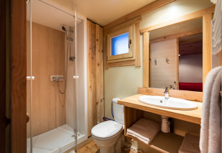 Badkamer bij een glamping-accommodatie met douche, toilet, houten details en een moderne wastafel.