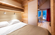Acogedora habitación de glamping con cama doble, paredes de madera y vista al bosque por grandes ventanas.