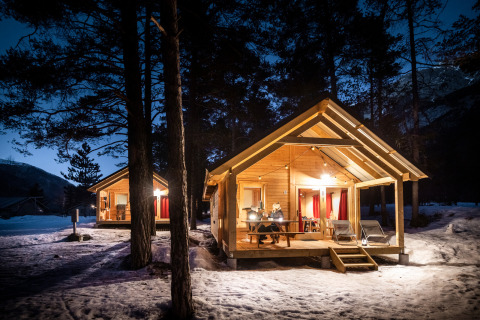 Cabañas de madera iluminadas en un bosque nevado al anochecer en Chalet Montana, Huttopia la Clarée, Francia.