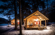 Beleuchtete Holzhütten im verschneiten Wald am Abend in Chalet Montana, Huttopia la Clarée, Frankreich.