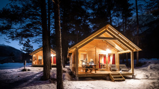 Beleuchtete Holzhütten im verschneiten Wald am Abend in Chalet Montana, Huttopia la Clarée, Frankreich.