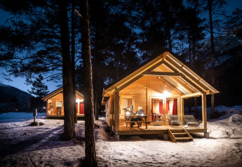 Beleuchtete Holzhütten im verschneiten Wald am Abend in Chalet Montana, Huttopia la Clarée, Frankreich.