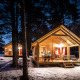 Verlichte houten chalets in een besneeuwd bos bij avond in Chalet Montana, Huttopia la Clarée, Frankrijk.