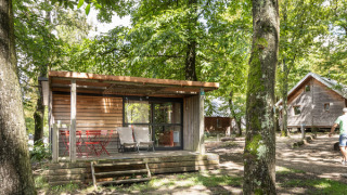 Træhytte ved navn Chalet Evasion i grøn skov ved Huttopia Versailles, Frankrig, med terrasse og stole.