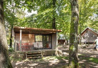 Træhytte ved navn Chalet Evasion i grøn skov ved Huttopia Versailles, Frankrig, med terrasse og stole.