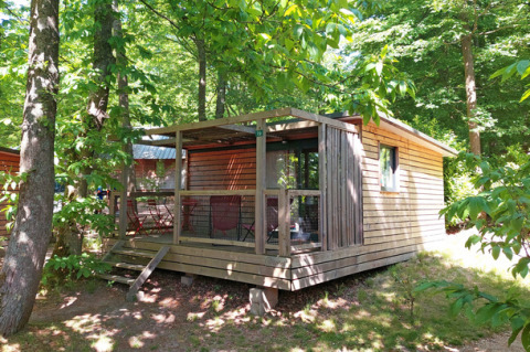 Cabaña Chalet Evasion en Huttopia Versailles, Francia, rodeada por árboles verdes y naturaleza exuberante.