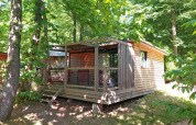 Cabaña Chalet Evasion en Huttopia Versailles, Francia, rodeada por árboles verdes y naturaleza exuberante.