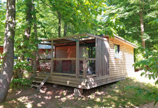 Cabaña Chalet Evasion en Huttopia Versailles, Francia, rodeada por árboles verdes y naturaleza exuberante.