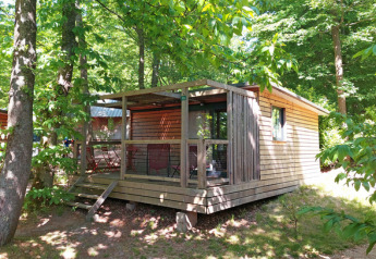 En træhytte kaldet Chalet Evasion ved Huttopia Versailles i Frankrig, omgivet af grønne træer og natur.