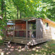 En træhytte kaldet Chalet Evasion ved Huttopia Versailles i Frankrig, omgivet af grønne træer og natur.
