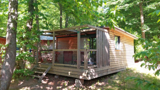 Cabaña Chalet Evasion en Huttopia Versailles, Francia, rodeada por árboles verdes y naturaleza exuberante.