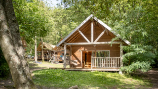 Blockhütte namens The cabin inmitten grüner Bäume, mit Veranda und ruhiger Atmosphäre im Wald.