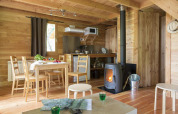 Cozy wooden cabin interior with dining table, wood stove, and kitchenette at Huttopia Versailles, France.