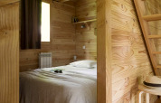 Gemütliches Schlafzimmer in einer Holzhütte bei Huttopia Versailles, Frankreich, mit Holzverkleidung.