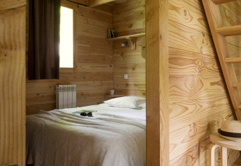 Camera accogliente nella cabina di Huttopia Versailles in Francia con pareti in legno e arredo minimalista.
