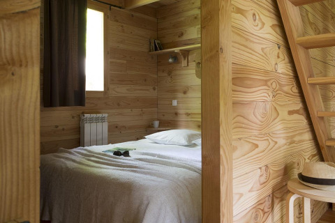 Acogedor dormitorio en la cabaña de Huttopia Versailles, Francia, con paredes de madera y decoración simple.