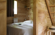 Chambre chaleureuse de la cabane à Huttopia Versailles, France, avec des murs en bois et déco épurée.