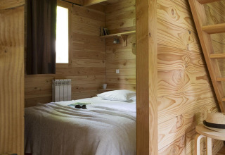 Chambre chaleureuse de la cabane à Huttopia Versailles, France, avec des murs en bois et déco épurée.