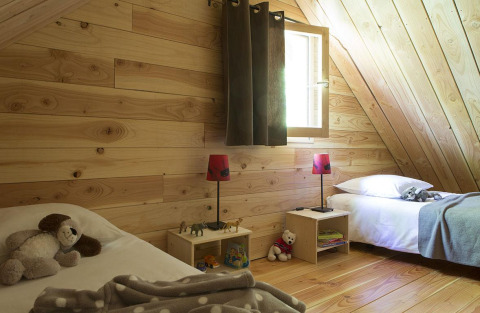Knusse houten slaapkamer met twee enkele bedden en speelgoed in The Cabin bij Huttopia Versailles, Frankrijk.