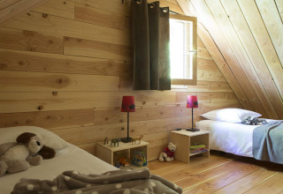 Cozy wooden bedroom with twin beds, toys, and soft lighting at The Cabin in Huttopia Versailles, France.