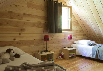 Camera in legno accogliente con due letti singoli e giocattoli, presso The Cabin a Huttopia Versailles, Francia.