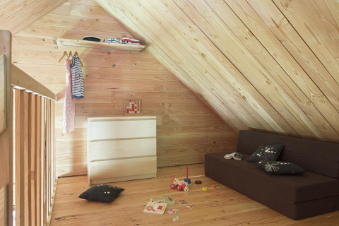 Et børneværelse med skrå loftpaneler i træ, en kommode, legetøj og en sofa i The cabin at Huttopia Versailles.