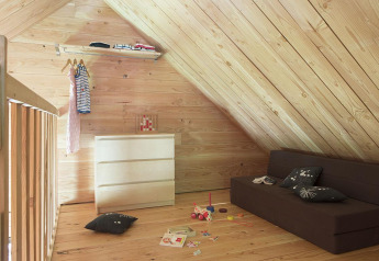 Gemütliches Dachzimmer mit Holzwänden, Sofa, Kommode und Kinderspielzeug in The Cabin at Huttopia Versailles.