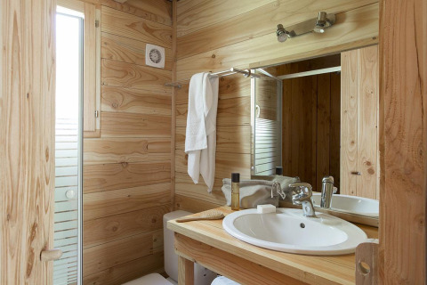 Salle de bain en bois à The Cabin de Huttopia Versailles, France, avec lavabo, miroir et serviette.