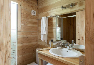 Baño de madera en The Cabin en Huttopia Versailles, Francia, con lavabo, espejo y toalla blanca.