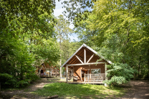 Chalets en bois dans une forêt verdoyante à Huttopia Versailles en France, parfaits pour se ressourcer.