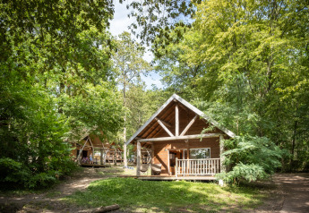 Chalets en bois dans une forêt verdoyante à Huttopia Versailles en France, parfaits pour se ressourcer.