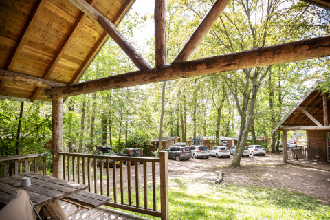 Vue depuis la terrasse d'une cabane à Huttopia Versailles, France, avec voitures garées et arbres autour.