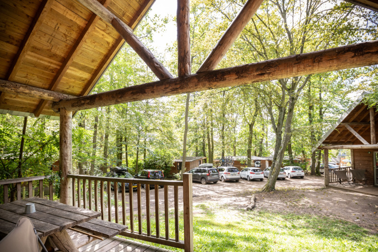 View from a cabin terrace at Huttopia Versailles in France, with parked cars and surrounding trees.