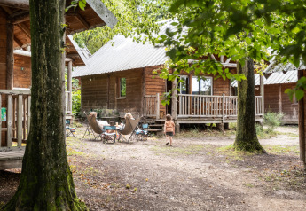 Des enfants jouent devant des cabanes en bois à Huttopia Versailles en France, entourés de forêt.