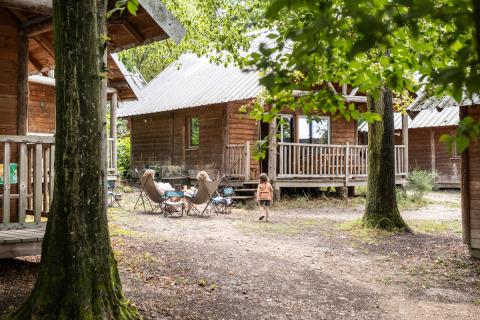 Des enfants jouent devant des cabanes en bois à Huttopia Versailles en France, entourés de forêt.