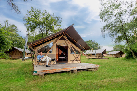 Een man ontspant voor een Trappeur tent II safaritent op een camping met meerdere soortgelijke tenten.