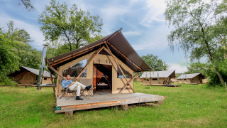 Un hombre se relaja frente a una tienda safari Trappeur tent II en un campamento con varias tiendas similares.