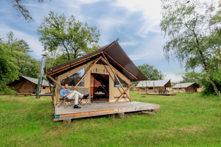 A man relaxes outside a Trappeur tent II safari tent on a glamping site with several similar tents.