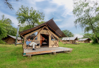 Un hombre se relaja frente a una tienda safari Trappeur tent II en un campamento con varias tiendas similares.